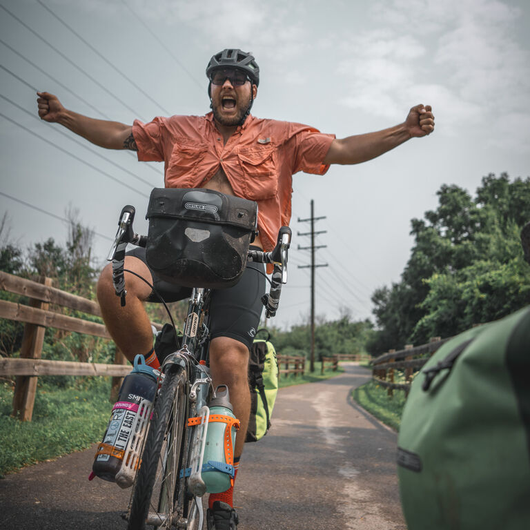 Adam Sauerwein on a bike on a trail, yelling in celebration with his arms and fists stretched out.