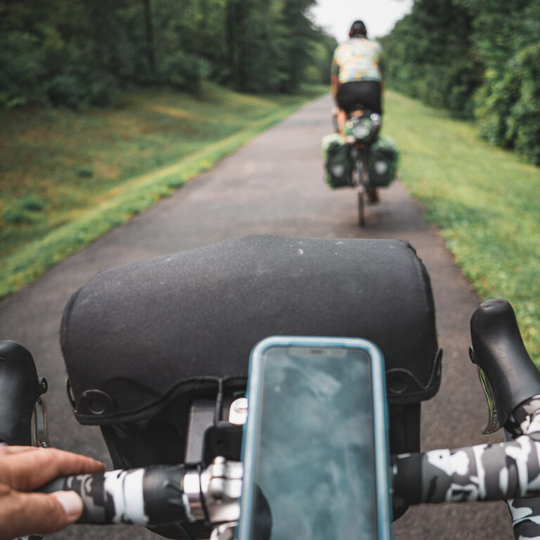 Adam Sauerwein bikes behind his friend on a trail, featuring his LifeProof phone case attached to his handlebars.