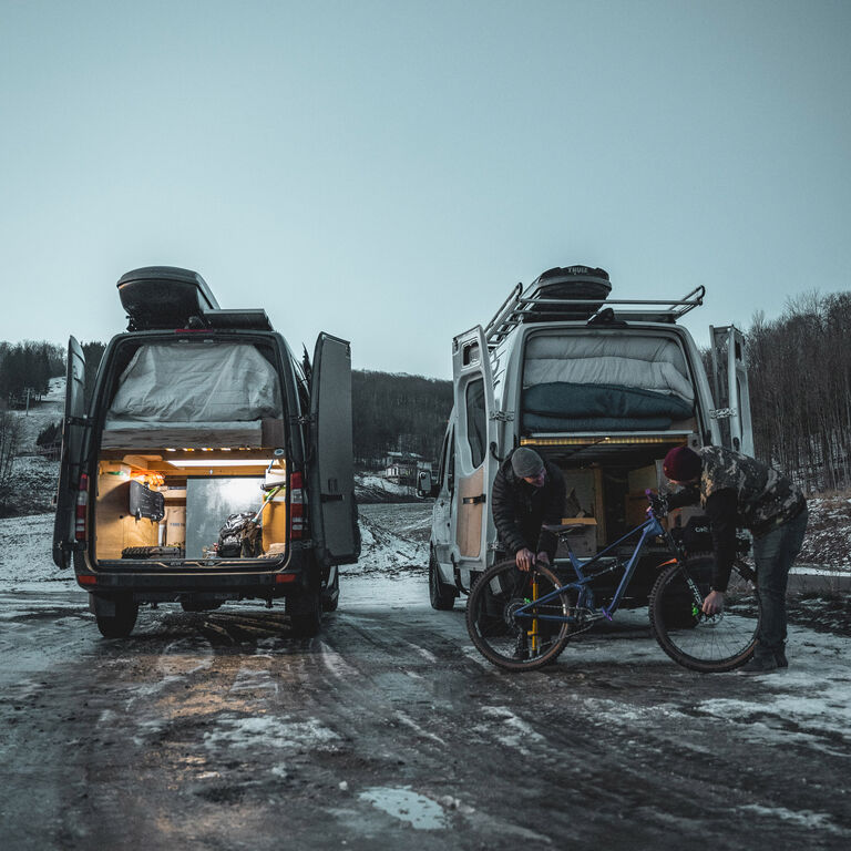 Adam Sauerwein and friend loading their bike into their sprinter vans on a snowy street.